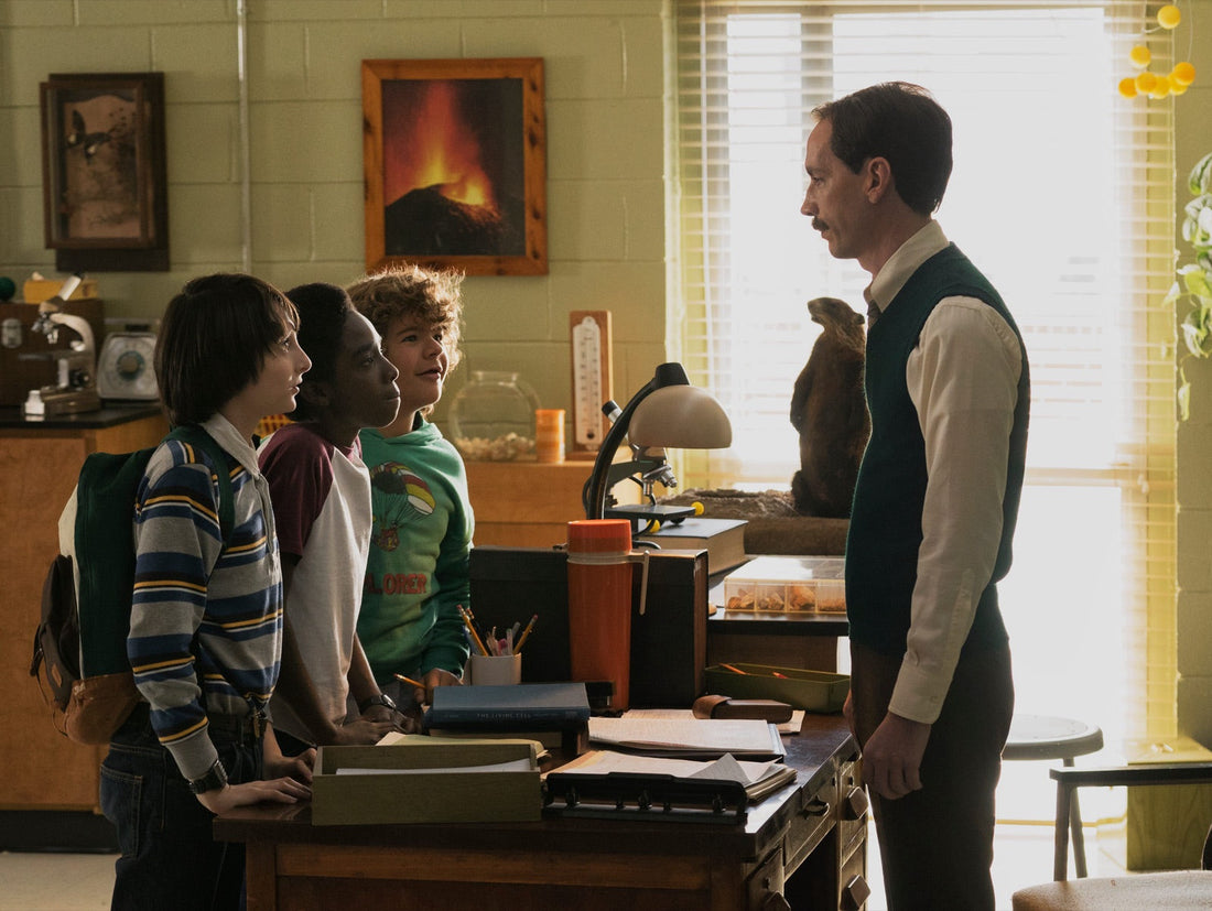 Meneer Clarke, in een groen vest, tegenover Mike, Lucas en Dustin in het wetenschapslokaal.